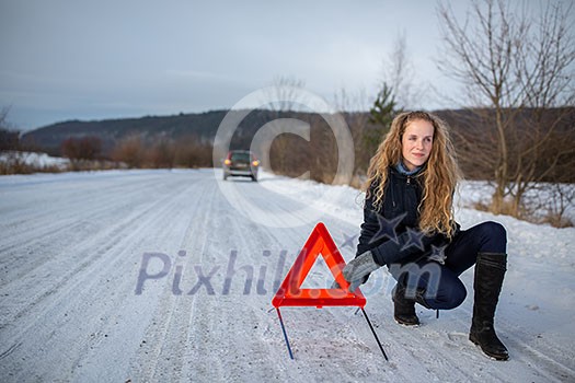 Young woman setting up a warning triangle and calling for assistance after her car broke down in the middle of nowhere on a freezing winter day Young woman setting up a warning triangle and calling for assistance after her car broke down in the middle of nowhere on a freezing winter day