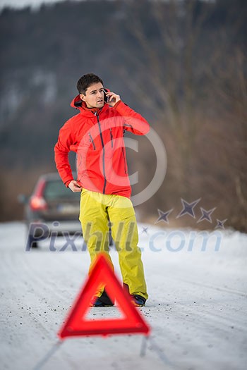 Young man setting up a warning triangle and calling for assistance after his car broke down in the middle of nowhere on a freezing winter day