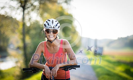 Pretty, young woman biking on a mountain bike enjoying healthy active lifestyle outdoors in summer (shallow DOF)