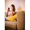 Cute young woman on a comfortable sofa in her modern apartment using her cell phone