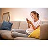 Cute young woman on a comfortable sofa in her modern apartment using her cell phone