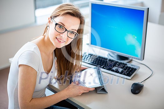 Smiling female student/ businesswoman using her tablet computer and a desktop computer, staying up to date, working, looking at the camera.