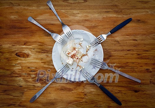 Top view on a plate with the remains of white cheese, 6 forks. Meal with friends.