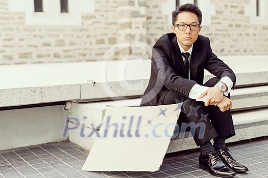 Businessman in a city street hsitting next to blank banner