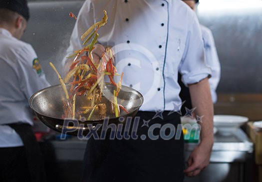 Young male chef flipping vegetables in wok at commercial kitchen Young male chef flipping vegetables in wok at commercial kitchen