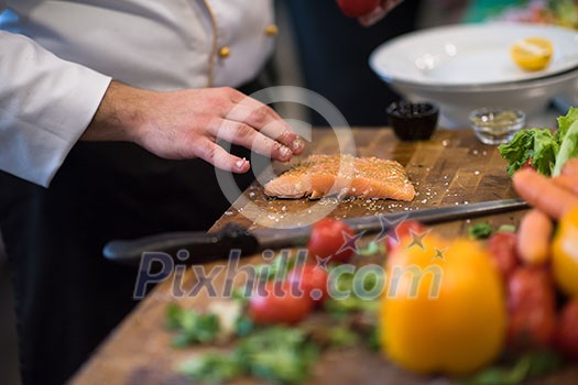 Chef hands preparing marinated Salmon fish fillet for frying in a restaurant kitchen