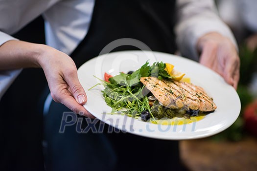 Chef hands holding fried Salmon fish fillet with vegetables for dinner in a restaurant kitchen