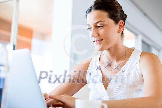 Young beautiful woman sitting at the table and working on her laptop