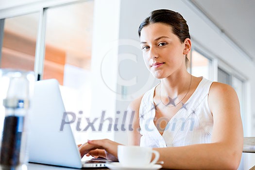 Young beautiful woman sitting at the table and working on her laptop Young beautiful woman sitting at the table and working on her laptop