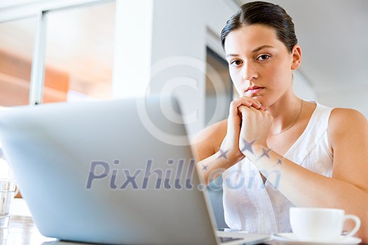 Young beautiful woman sitting at the table and working on her laptop Young beautiful woman sitting at the table and working on her laptop