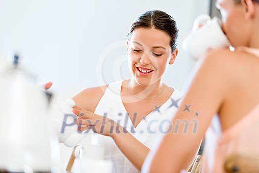 Young woman sitting at the kitchen table having tea with her friend Young woman sitting at the kitchen table having tea with her friend