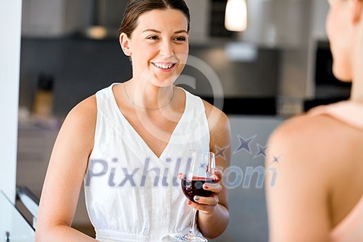 Young woman standing and talking to her friend with a glass of red wine