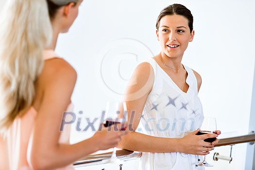 Young woman standing and talking to her friend with a glass of red wine