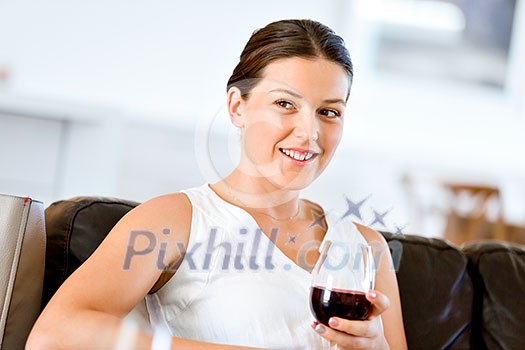 Beautiful young woman holding glass with red wine and smiling while sitting