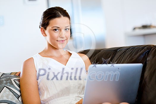 Young beautiful woman sitting on the sofa and working on her laptop