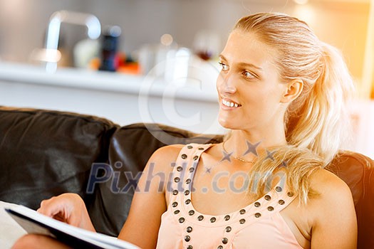 Happy woman reading a magazine sitting on a sofa in the living room at home