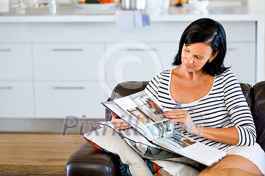 Happy woman reading book sitting on a sofa in the living room at home