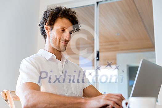 Young man in casual clothes working on laptop at home