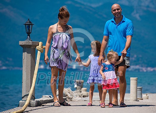 young happy family with cute little daughters holding their hands while walking by the sea during Summer vacation  Healthy family holiday concept