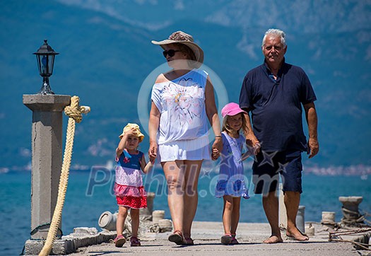 happy grandparents with cute little granddaughters having fun holding their hands while walking  by the sea during Summer vacation  Healthy family holiday concept