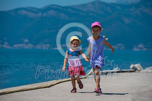 Happy smiling little sisters having fun holding their hands while running on the beach coast during Summer vacation  Healthy childhood lifestyle concept