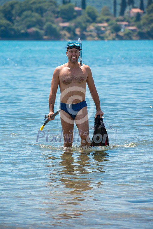 Young smiling fisherman with equipment standing in the shallow water of the sea while preparing for underwater fishing  active holiday concept