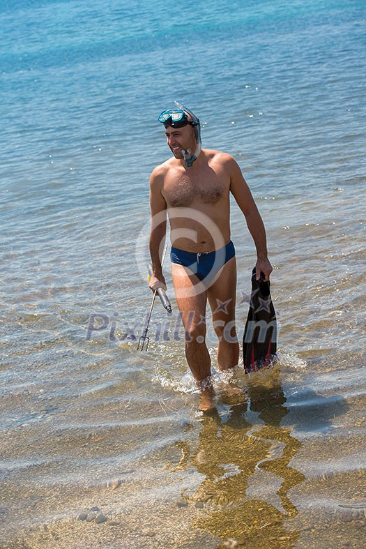 Young smiling fisherman with equipment standing in the shallow water of the sea while preparing for underwater fishing active holiday concept Young smiling fisherman with equipment standing in the shallow water of the sea while preparing for underwater fishing active holiday concept