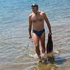 Young smiling fisherman with equipment standing in the shallow water of the sea while preparing for underwater fishing  active holiday concept