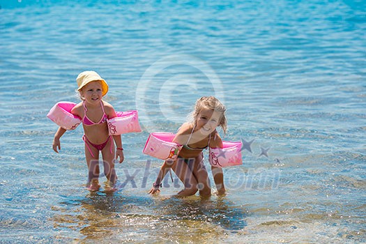 two happy little girls with swimming armbands playing in shallow water of the sea during Summer vacation  Healthy childhood lifestyle concept