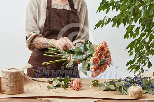 Girl florist is decorating beautiful bouquet from fresh natural roses step by step at the table with paper and rope on it. Mother's Day holiday. Girl florist is decorating beautiful bouquet from fresh natural roses step by step at the table with paper and rope on it. Mother's Day holiday.