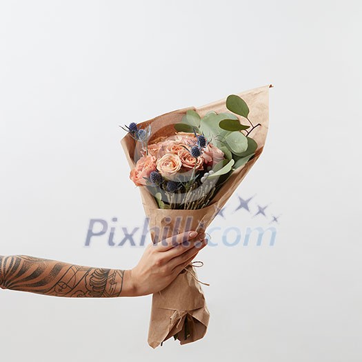 Woman's hand holds beautiful colourful blossoming flower bouquet of fresh roses living coral color on a light background. Place for text. Mother's Day.