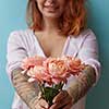 A happy red-haired woman with a tattoo holds in her hands delicate pink roses on a blue background with copy space for text. Holiday gift concept