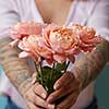 A girl with a tattoo holds a beautiful bouquet of pink roses around a blue background with copy space. Mother's Day Gift