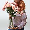 A woman with a tattoo holding a large bouquet of pink roses in a glass vase around a gray background with copy space. Mother's Day Gift