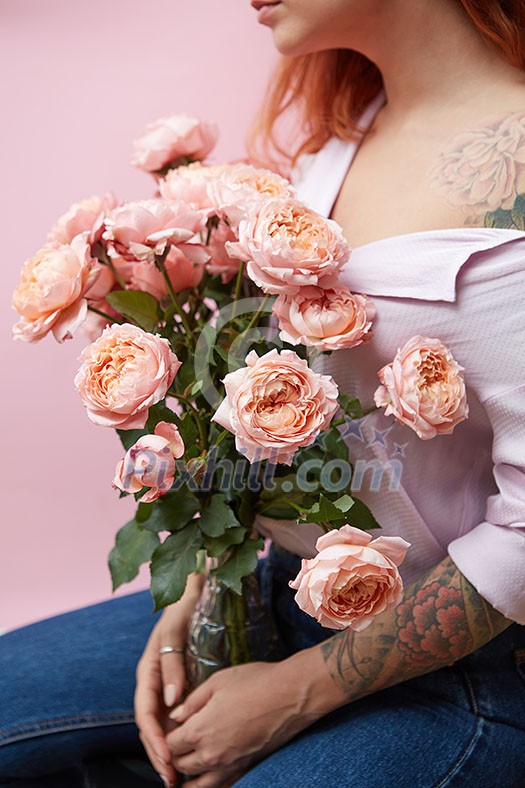 A bouquet of pink roses in a vase holds a girl with a tattoo on a pink background with copy space. St. Valentine's Day