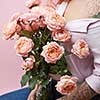 A bouquet of pink roses in a vase holds a girl with a tattoo on a pink background with copy space. St. Valentine's Day