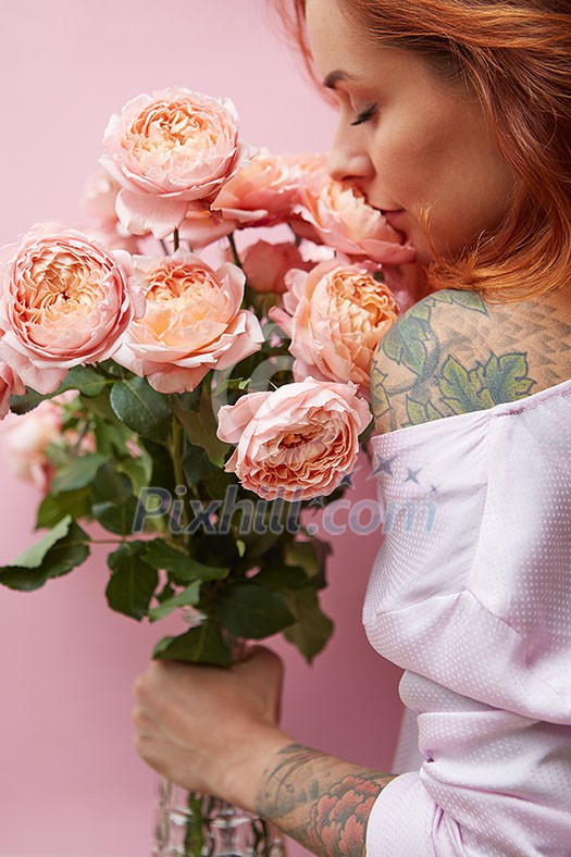 Wonderful summer fresh roses living coral colored as a greeting bouquet in a female's hand with tattoo on a coral background. Place for text. Gift for Mother's Day.