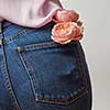 Beautiful female butt in jeans with fresh roses of coral living color in a back pocket on a light gray background. Place for text.