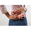 Young girl wearing of jeans pants and pink shirt from back put in natural flowers roses in a pocket on a gray background, place for text. Concept of Woman's or Mother's Day.