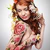 Red-haired girl with a floral tattoo and red hair decorated with flowers around a gray background with copy space. Spring layout