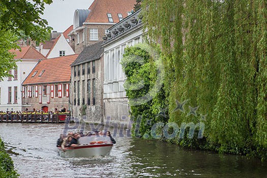 Bruges, Belgium - May 17, 2012: Water channel with old trees houses, a cafe terrace and a motor boat on a spring day.Picturesque landscape.