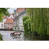 Bruges, Belgium - May 17, 2012: Water channel with old trees houses, a cafe terrace and a motor boat on a spring day.Picturesque landscape.