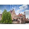 Bruges, Belgium - May 17, 2012: Water channel with old houses, a bell tower in the background and a cafe on a spring day against the blue sky.