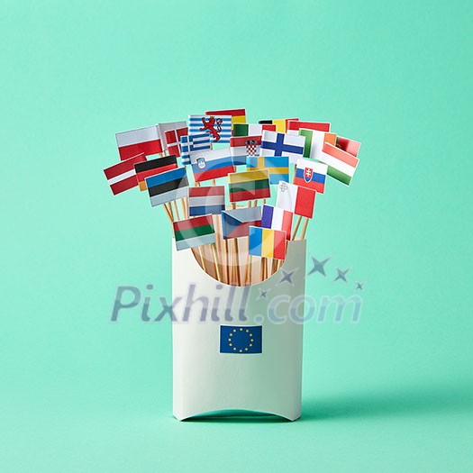 In a cardboard box with sign of the European Union, collection of paper flags of European Union countries on green background . Economic, Political Union of European States
