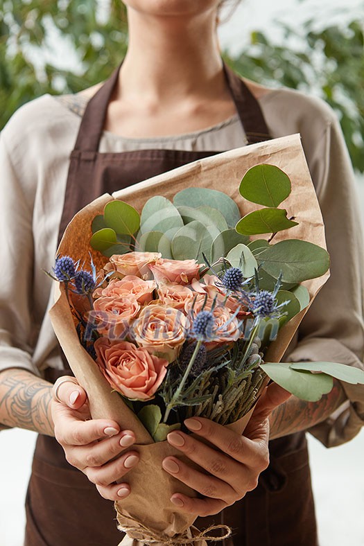 Florist woman with a bouquet of coral roses and green leaf. Girl is holding a flowers in her hands. The gift to Mother's Day.