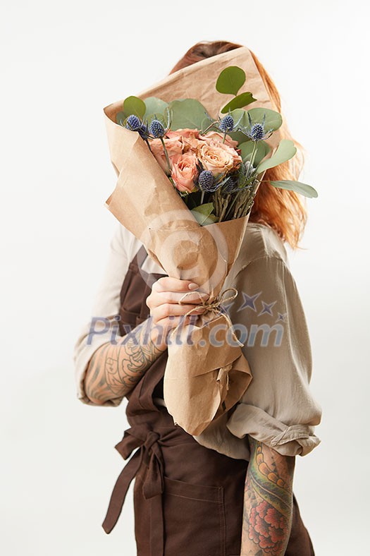 Delicate flowers coral living roses and eryngium as a beautiful bouquet hide girl's face and ginger hair on a gray background, place for text. Concept of Mother's or Woman's Day.