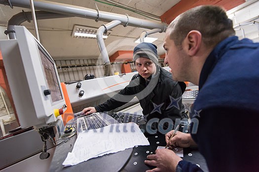 two young carpenters calculating and programming a cnc wood working machine in workshop. wood workers preparing a computer program for CNC machine at big modern carpentry