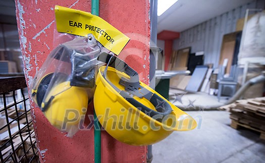 standard security equipment yellow helmet and ears protection hanging on the wall at production Department of a big modern wooden furniture factory