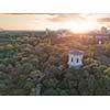 A city in the distance and a green park with a tower and people on the roof against the sky with the sunset. Aerial view from the drone