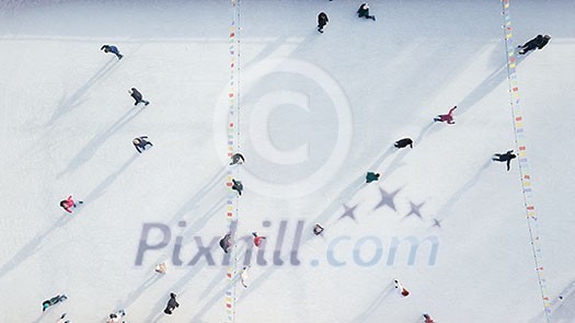 Outdoor ice skating rink with people riding on a winter day. Aerial view from the drone.